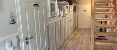 A hallway with a wooden staircase, a white door, and a shelf with decorative items.
