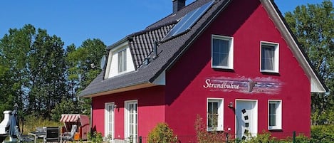 A red house with a sloped roof, solar panels, and a fenced yard with outdoor furniture.