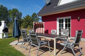 A patio with a table and chairs, a barbecue grill, and a satellite dish on a house with a red exterior. - Holiday home with 3 bedrooms (Glowe\/Rügen)