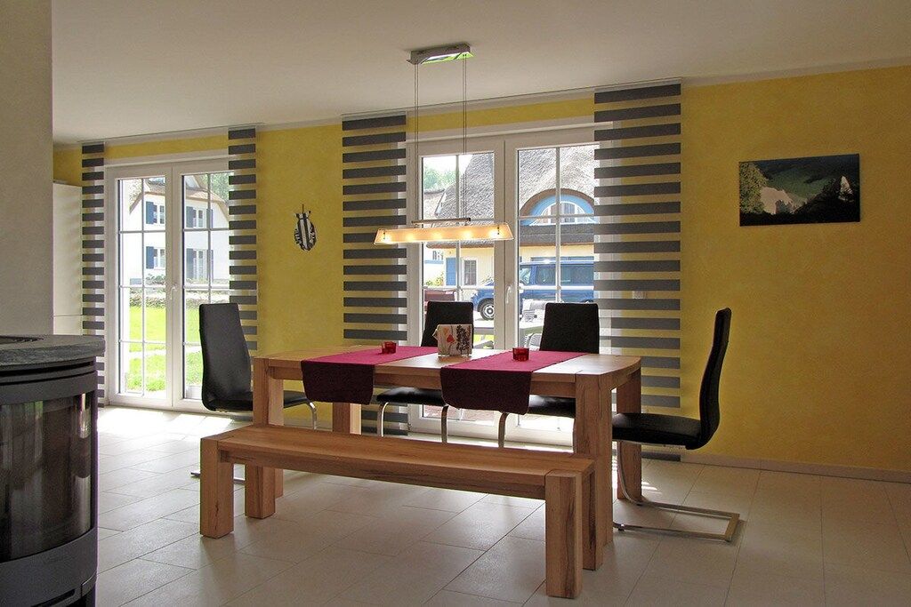 Een eethoek met een tafel, stoelen, een bank, een fornuis en uitzicht door de ramen.