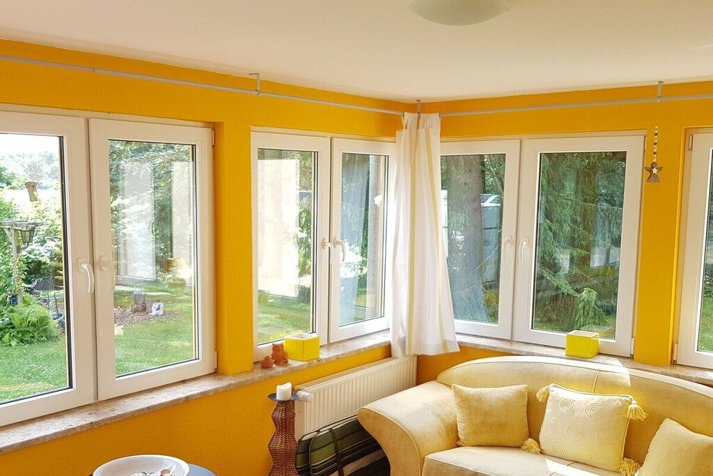 Ein Zimmer mit einer gelben Wand, einem weißen Heizkörper, einem beigefarbenen Sofa und einem Fenster mit Vorhang.