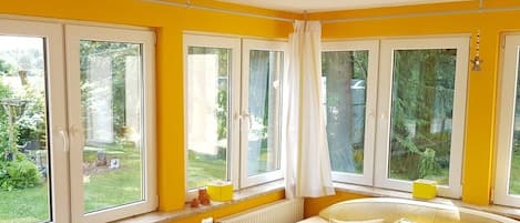 Ein Zimmer mit einer gelben Wand, einem weißen Heizkörper, einem beigefarbenen Sofa und einem Fenster mit Vorhang.