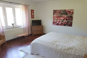 A bedroom with a bed, a television on a wooden dresser, a window with curtains, and a wall-mounted power outlet. - Eldenholz on the Reeck Canal (Waren)