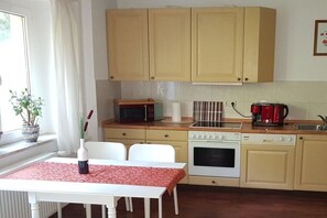 A compact kitchen with a microwave, stove, and coffee maker. There is a dining table with chairs and a window with curtains. - Eldenholz on the Reeck Canal (Waren)
