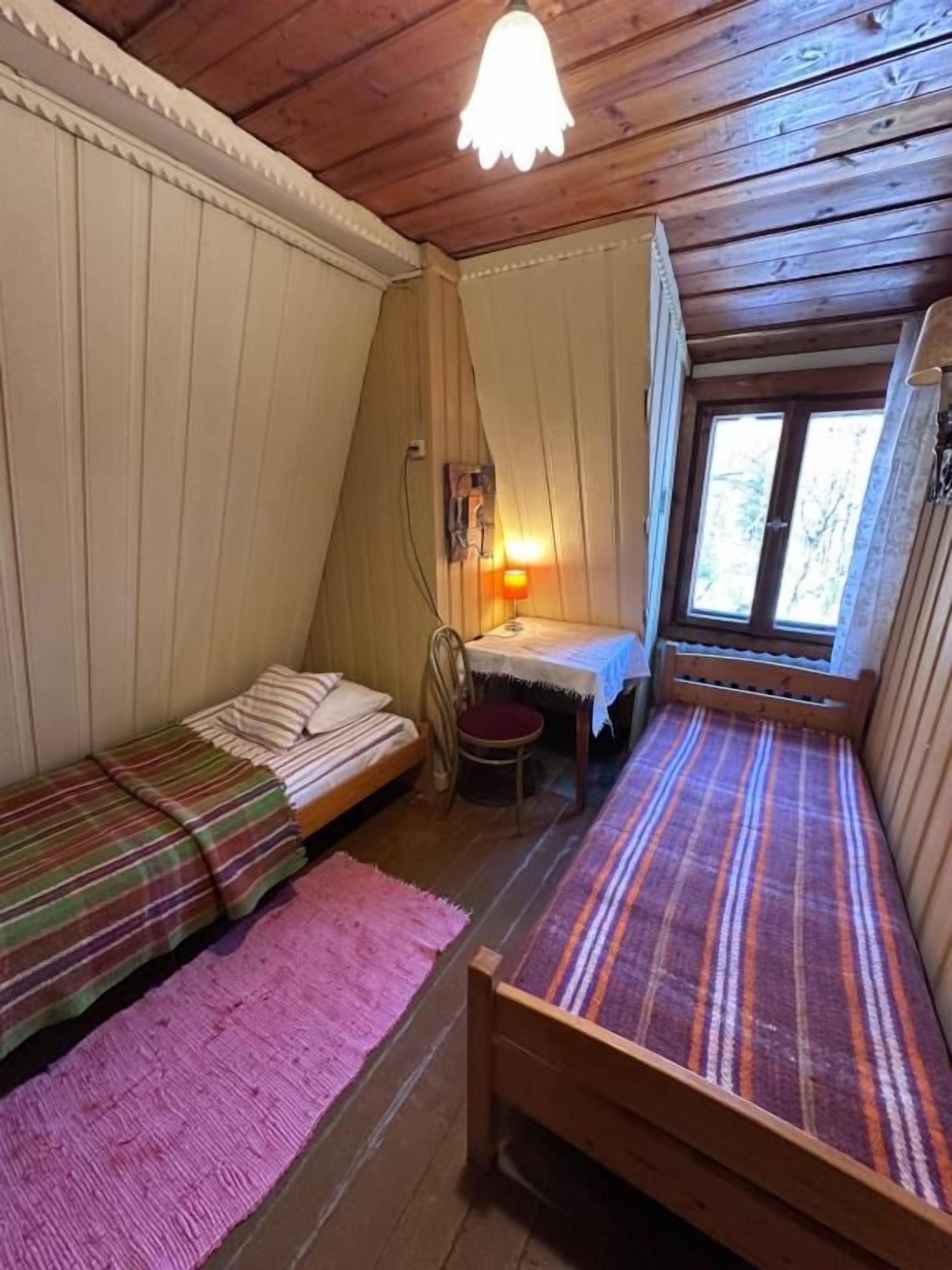 Ein Zimmer mit zwei Holzbetten, einem kleinen Tisch, einem Stuhl und einem Fenster.