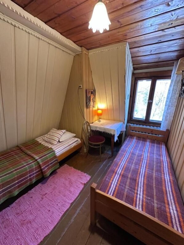 A room with two wooden beds, a small table, a chair, and a window.