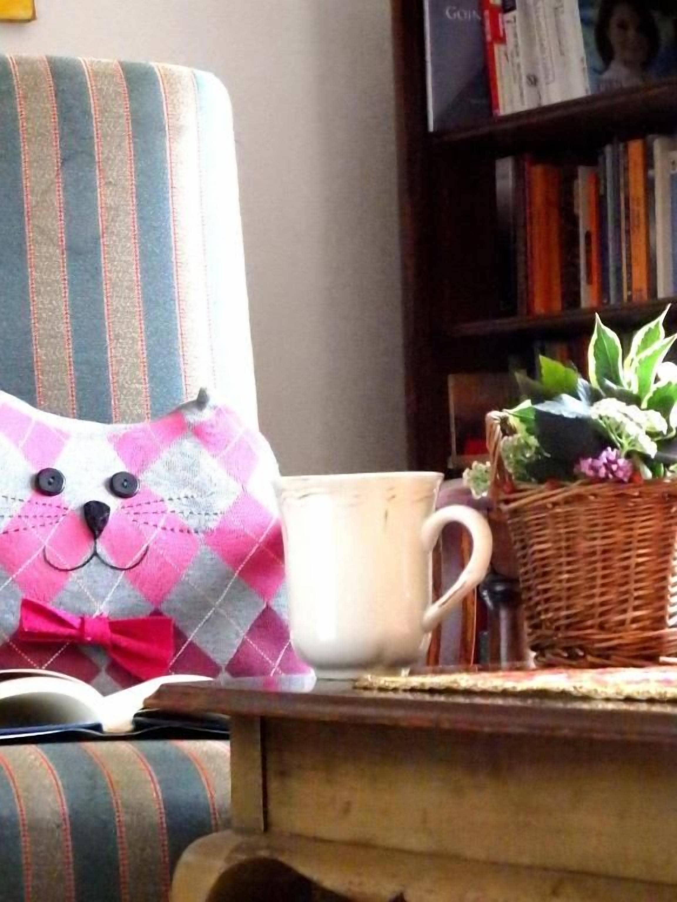 Un fauteuil à rayures, un coussin, une tasse et un panier en osier contenant une plante, le tout posé sur une table en bois.