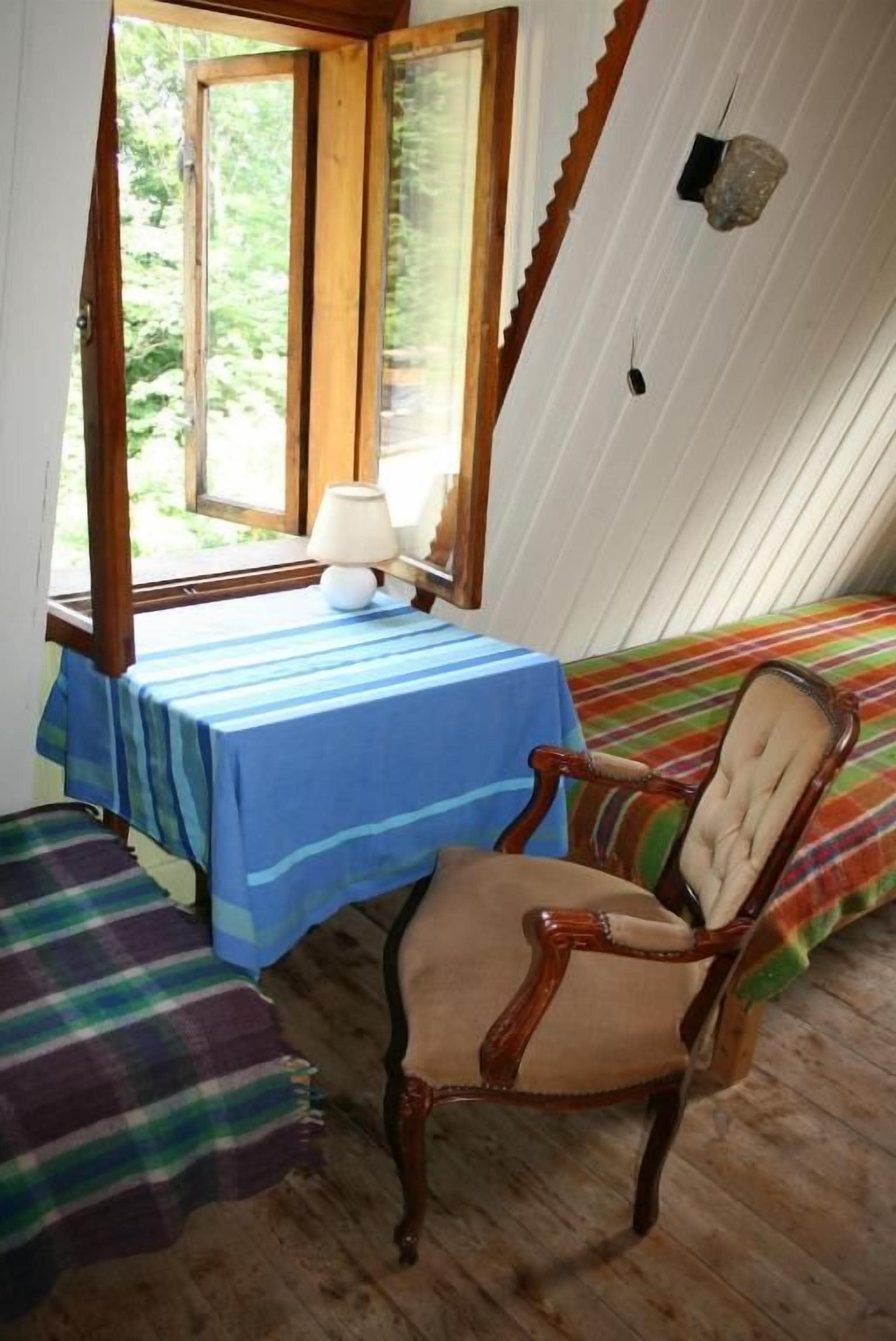Una habitación con una cama, una mesa con lámpara, una silla y una ventana con vistas a zonas verdes.