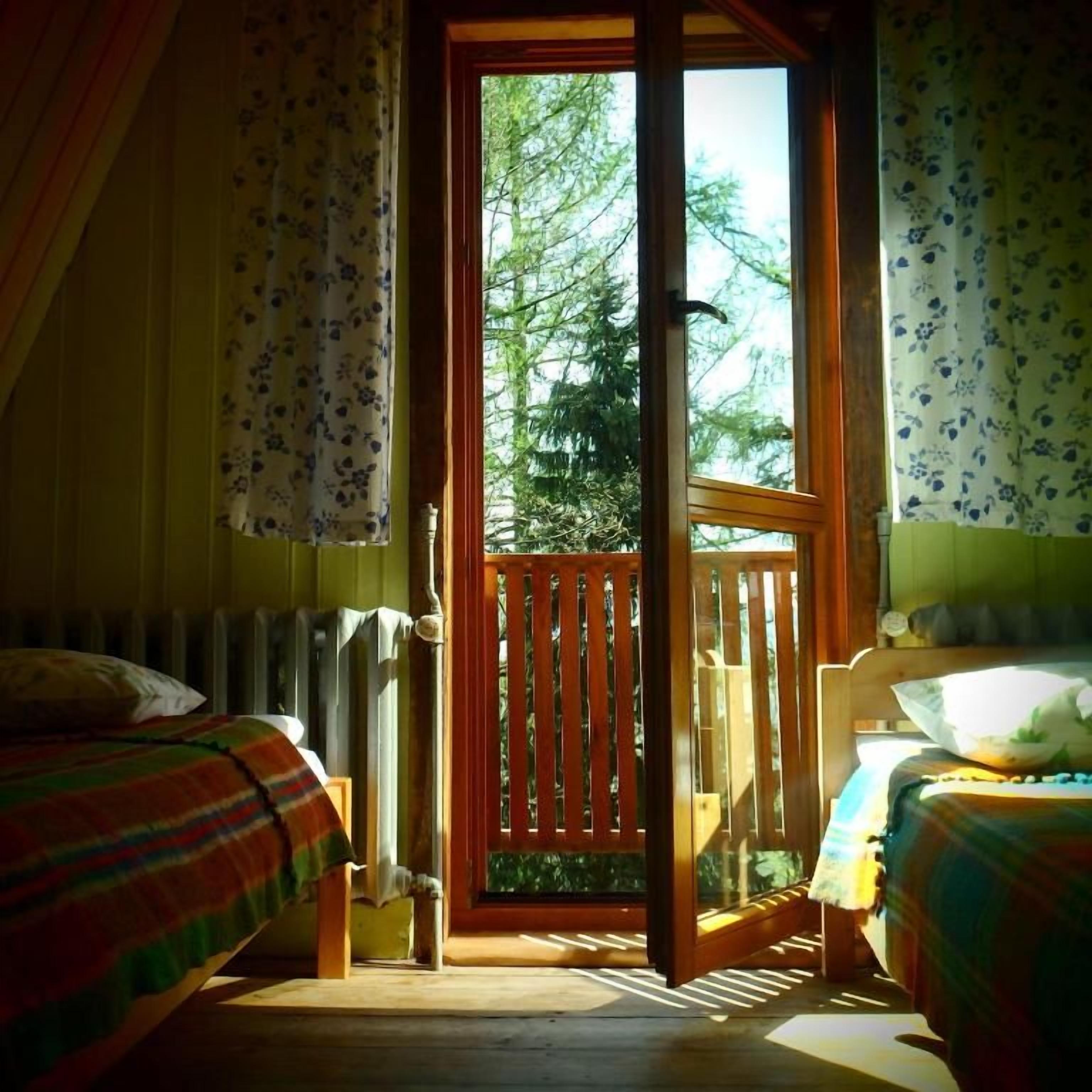Quarto com duas camas, varanda de madeira e vista para árvores através de uma porta aberta.
