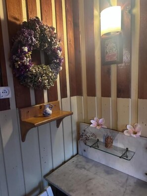 A room with wooden paneling, a wall-mounted light fixture, a shelf with a ceramic pitcher, and a small table with a glass top.