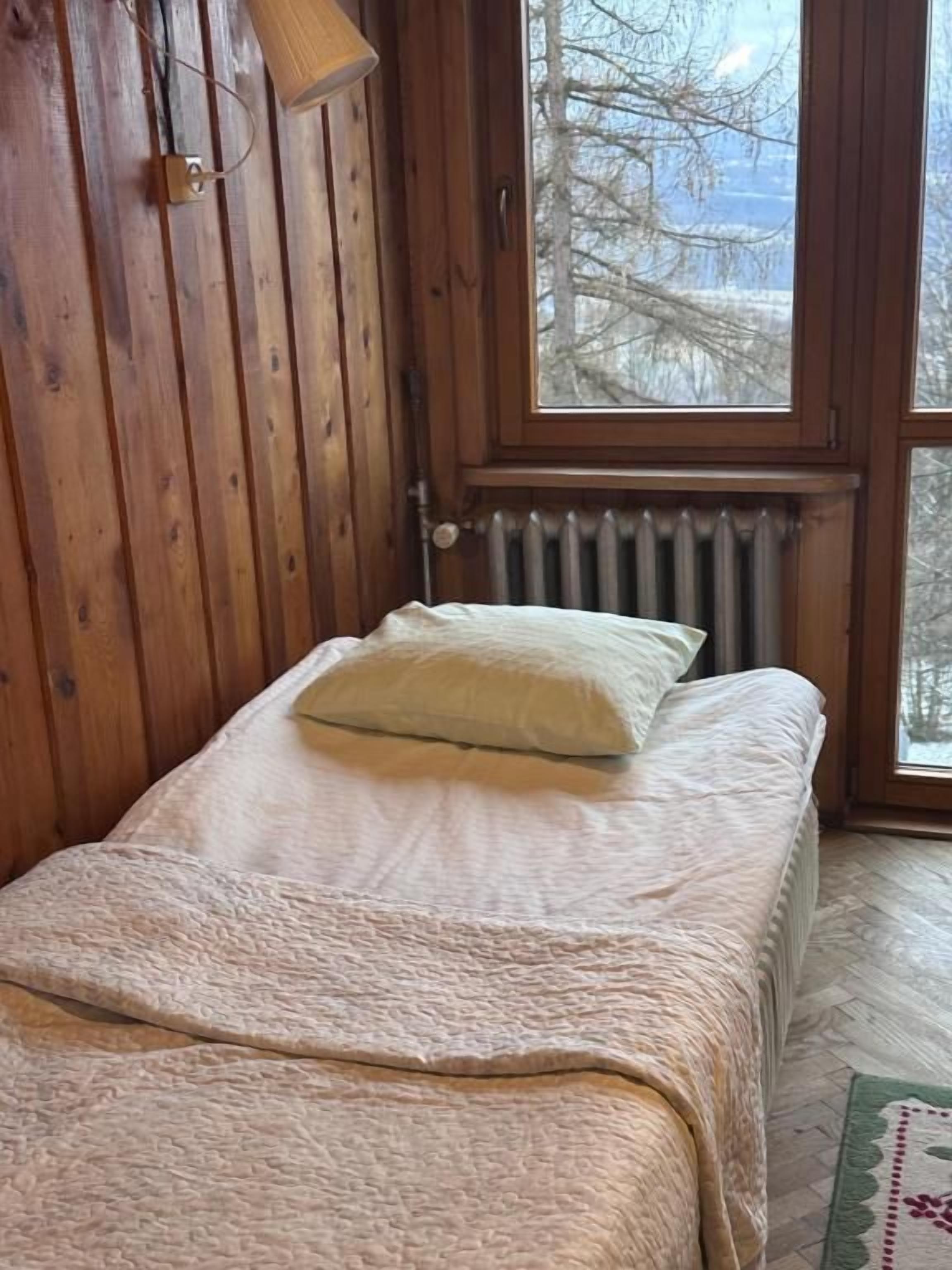 A wooden cabin room with a bed, a window, and a radiator.