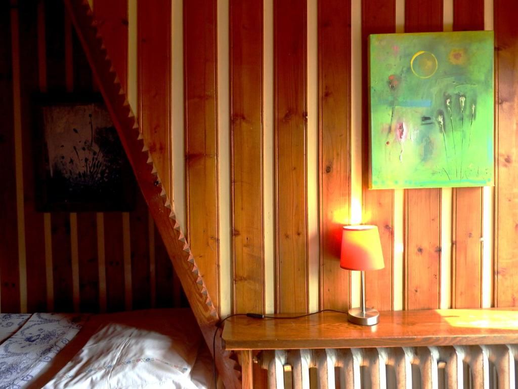 Una habitación de madera con una cama, un radiador, una lámpara y un cuadro en la pared.