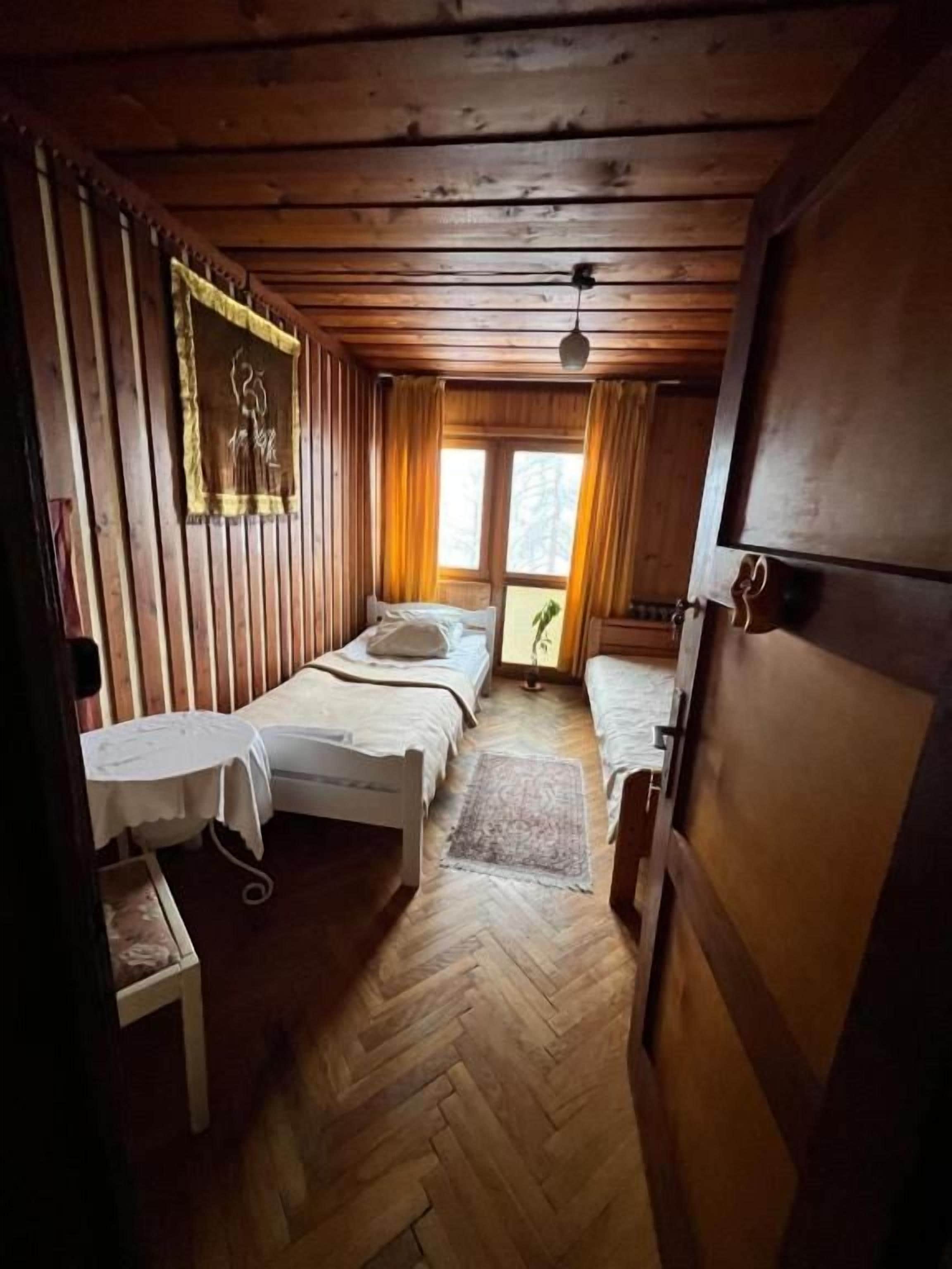 A wooden cabin room with two beds, a small table, and a window.