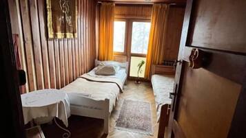 A wooden cabin room with two beds, a small table, and a window.