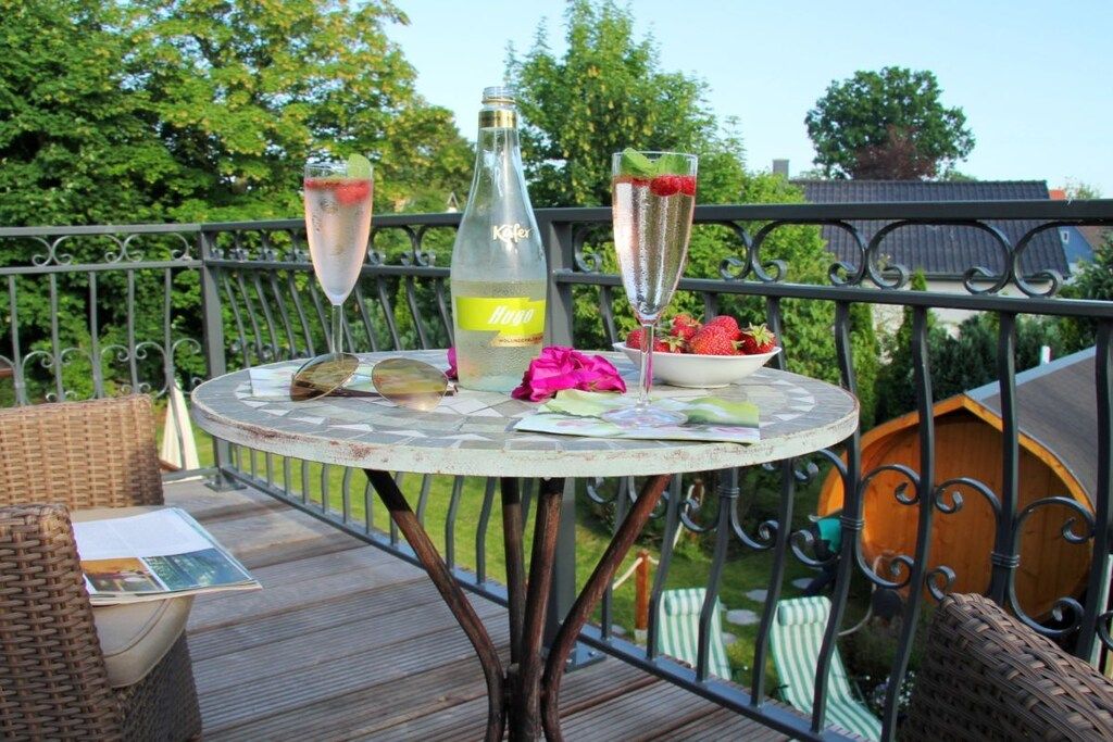A round table with a bottle and two glasses on a balcony.