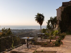 An outdoor patio with a table and chairs, a palm tree, and a view of the ocean. - Holiday Apartment With 1 Bedroom (Diano Castello)