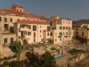 A coastal town with terracotta-roofed buildings, a stone wall, and a swimming pool. - Holiday Apartment With 1 Bedroom (Diano Castello)