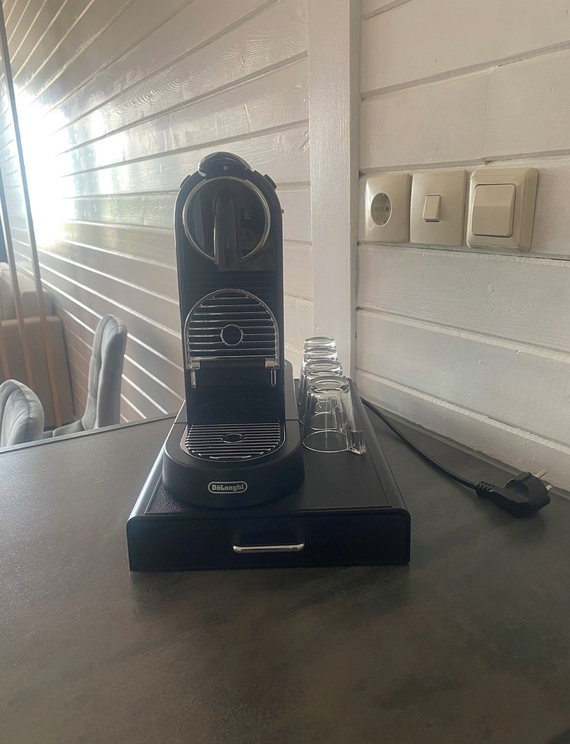 A DeLonghi espresso machine on a table with a window in the background.