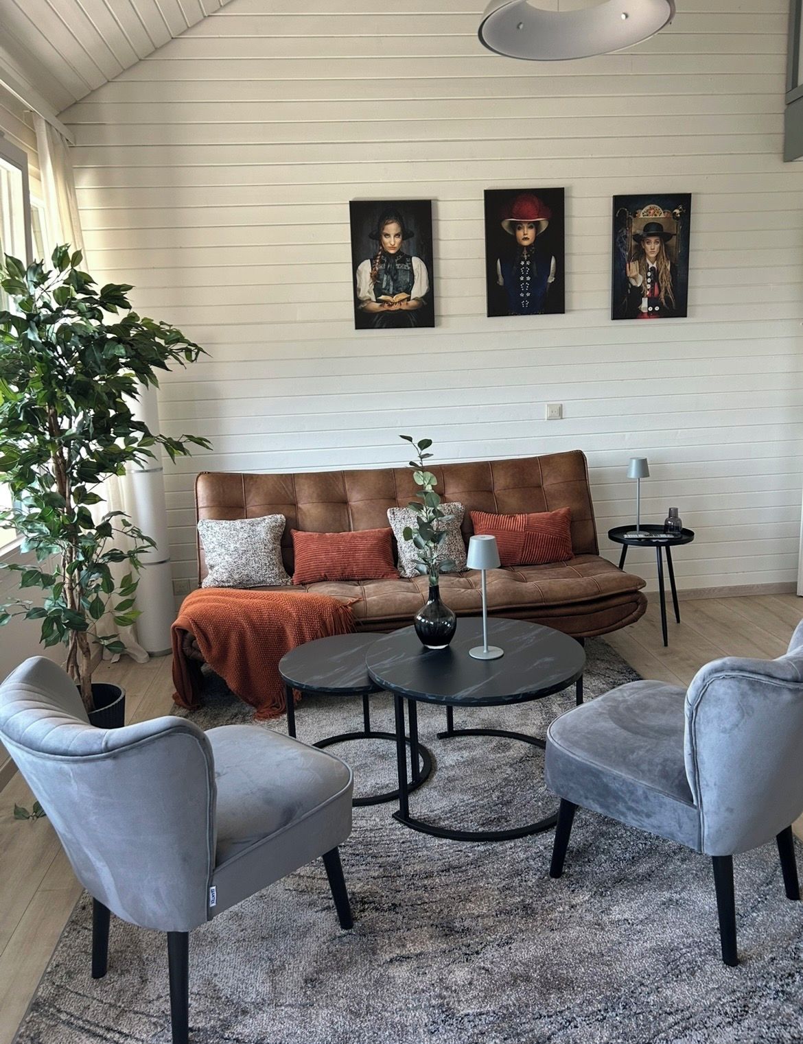 Ein Wohnzimmer mit einem braunen Ledersofa, zwei grauen Sessel, einem runden Couchtisch und einem Topfpflanze.