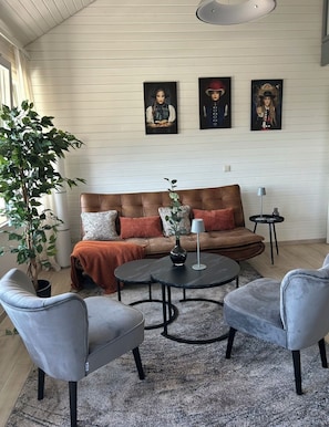 Un salon avec un canapé en cuir marron, deux fauteuils gris, une table basse ronde et une plante en pot.