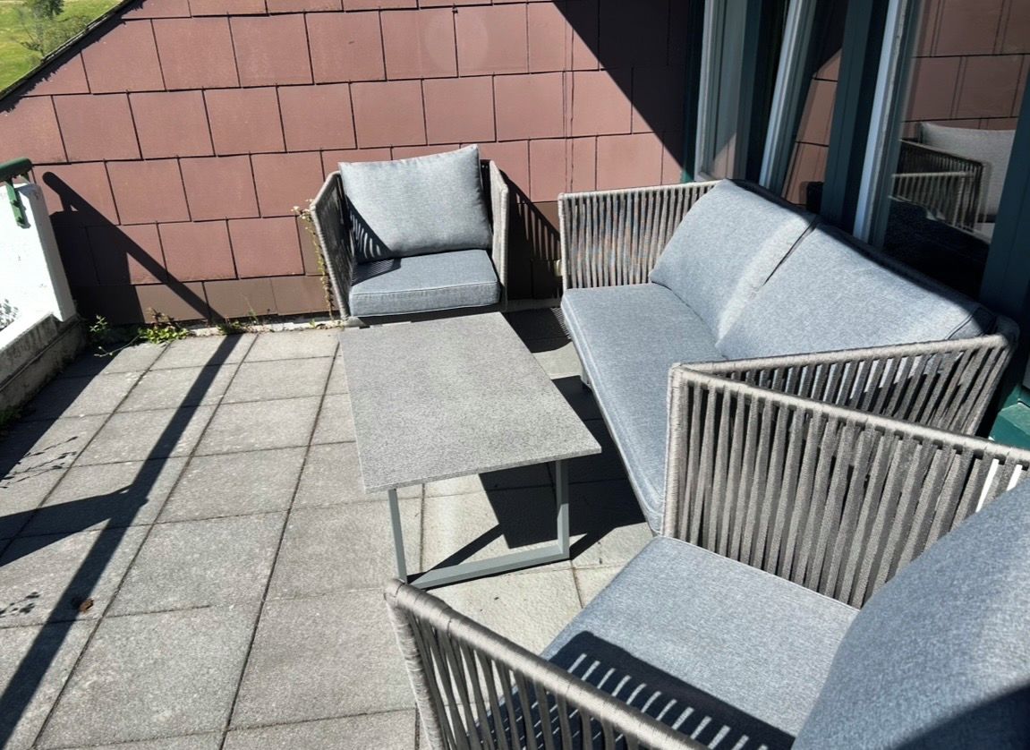 Eine Terrasse mit Gartenmöbeln, darunter eine Couch und Stühle, an einer Ziegelwand.