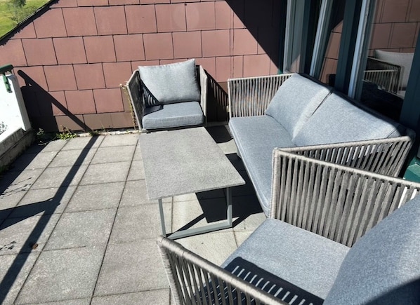 Un espace patio aménagé avec du mobilier d’extérieur, notamment un canapé et des fauteuils, adossé à un mur en briques.