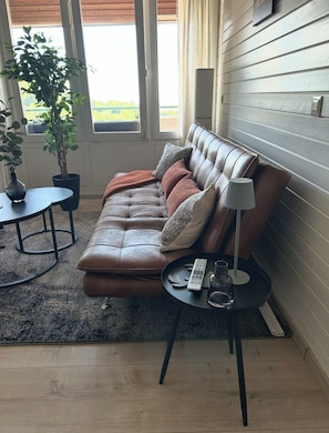 Un salon chaleureux avec un canapé en cuir, une table d’appoint, un lampadaire et une plante en pot.