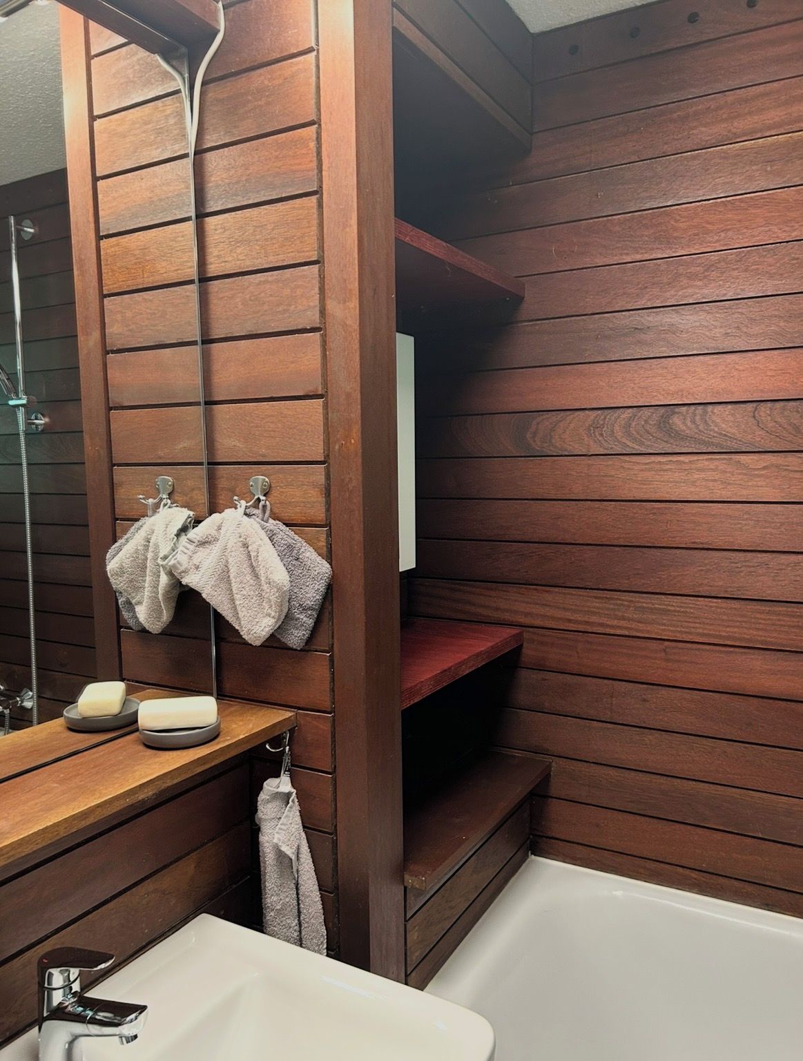 Une salle de bain avec des lambris en bois, un miroir, un lavabo et une douche.