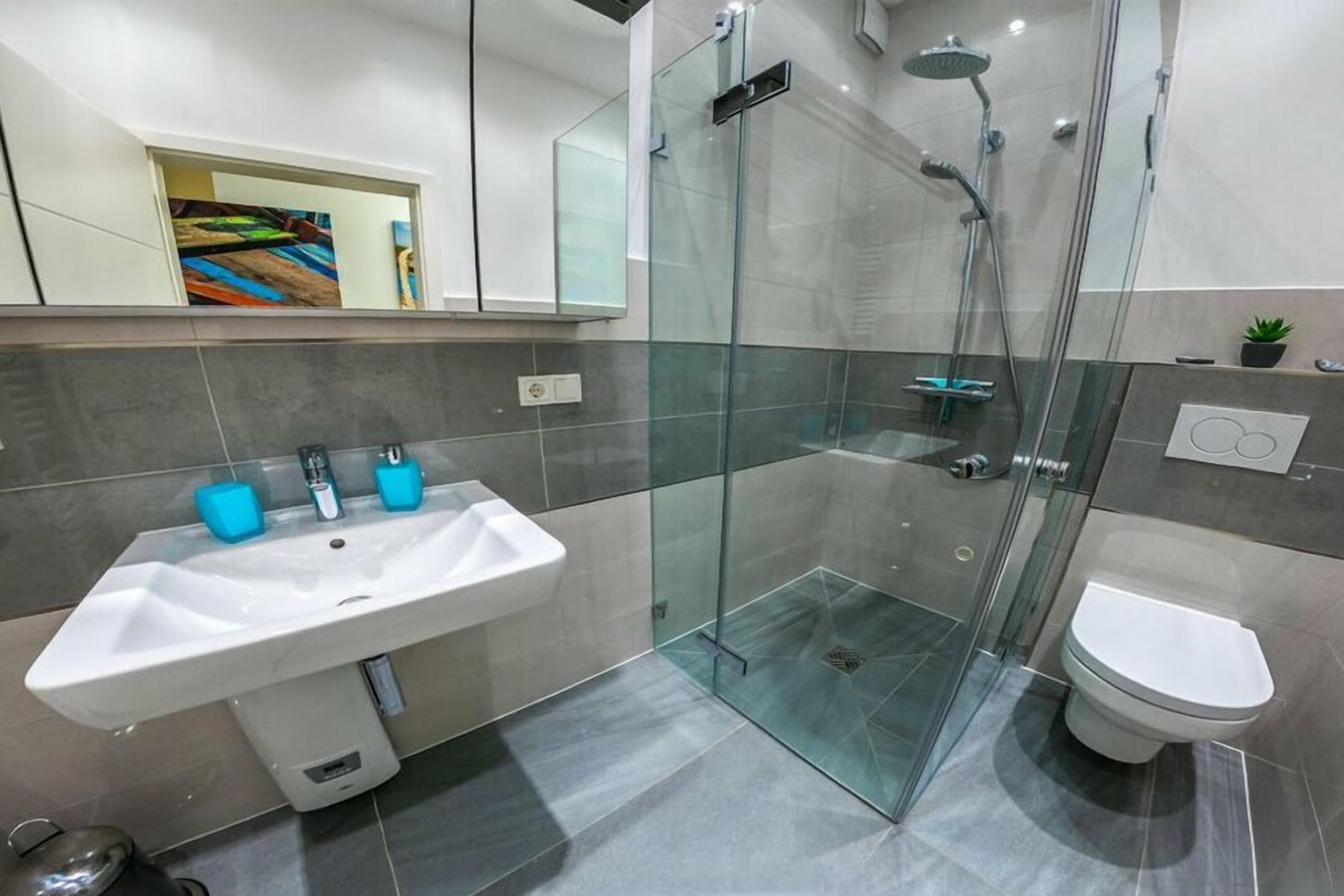 Une salle de bain moderne avec une douche à parois de verre, un lavabo blanc doté de deux distributeurs de savon bleus et des toilettes.
