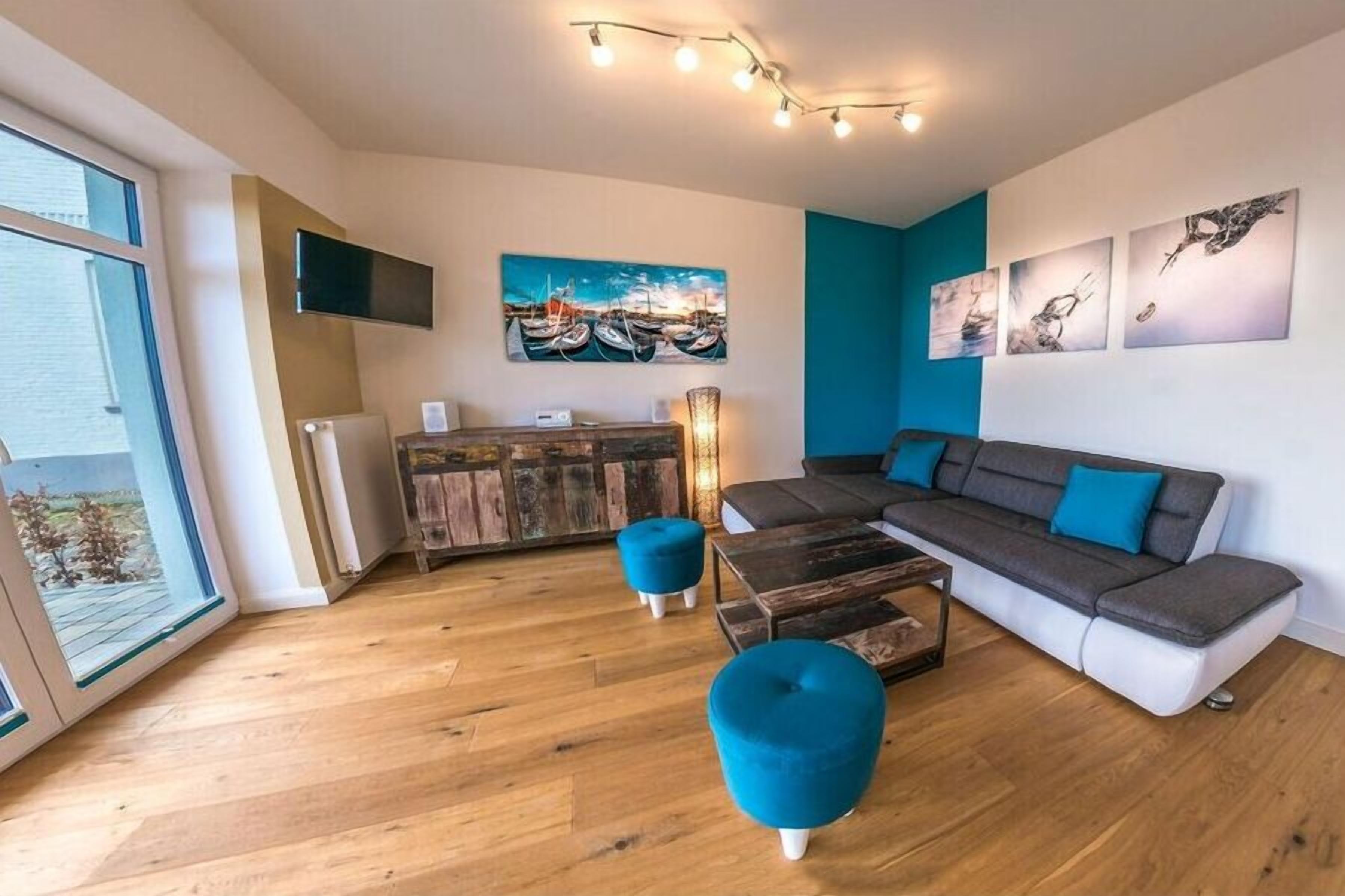 Ein modernes Wohnzimmer mit einer Couch, Hocker, einem Flachbildfernseher und Kunstwerken an den Wänden.