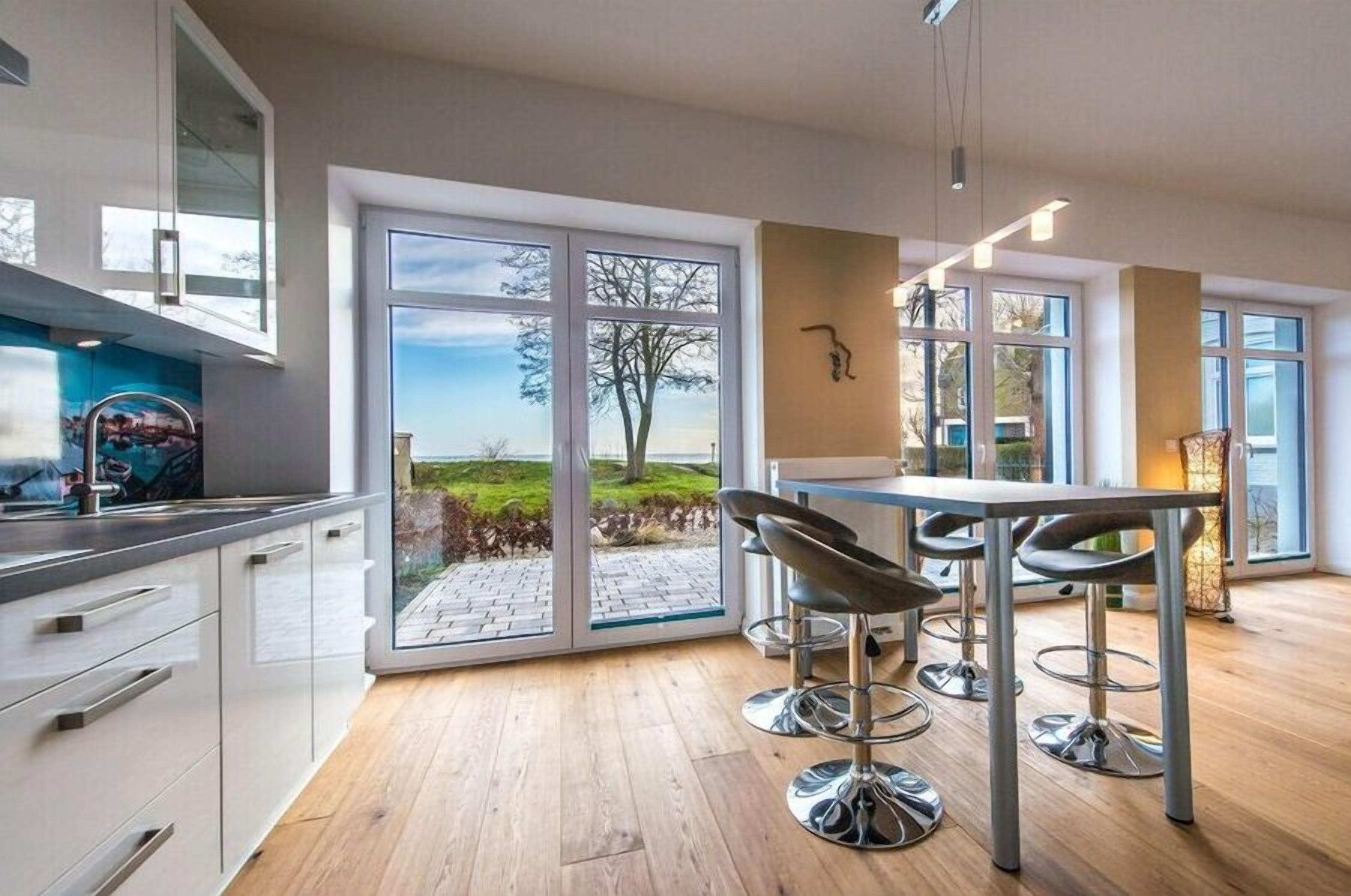 A modern kitchen with large windows, a dining area with bar stools, and a view of the outdoors.
