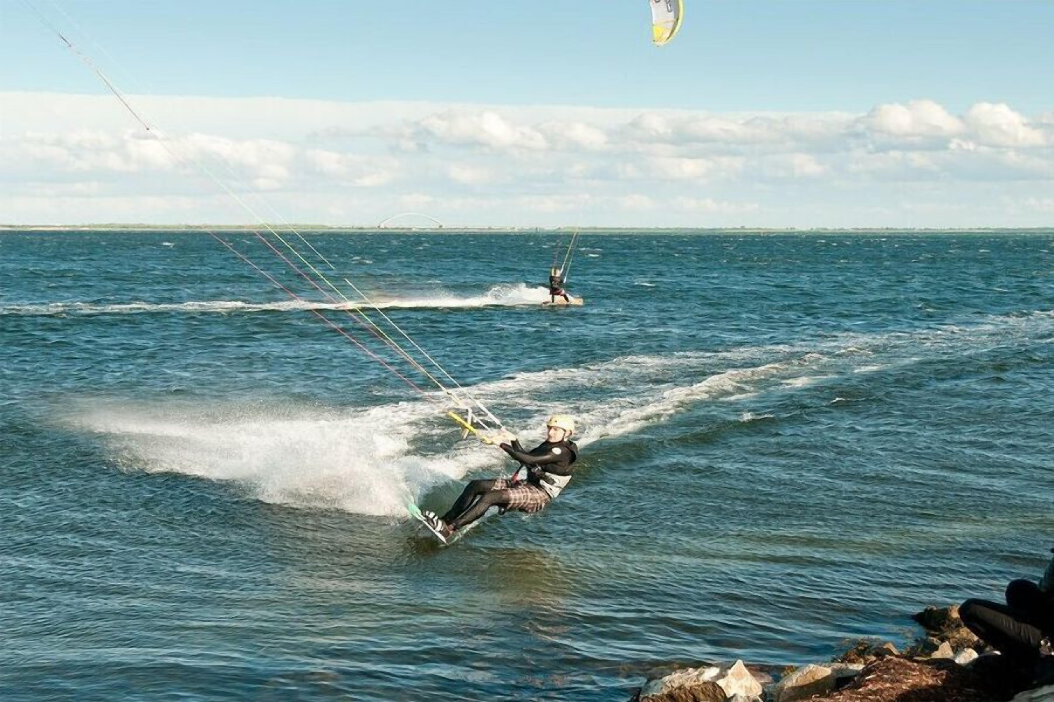 Eine Person windsurft auf dem Wasser, im Hintergrund ist ein klarer Himmel zu sehen.