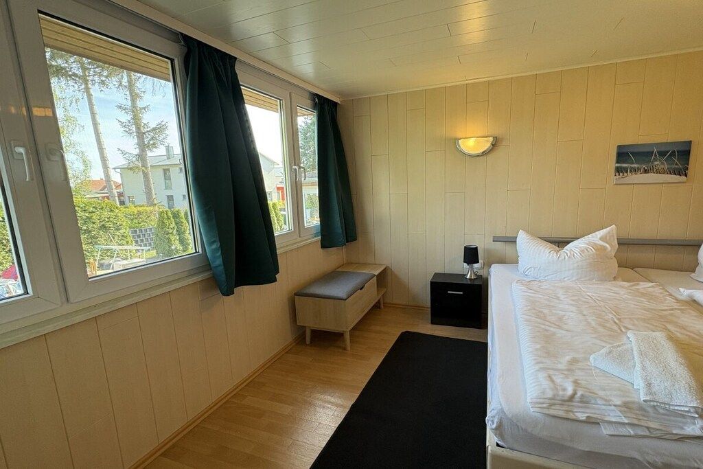A bedroom with a bed, bedside table, bench, and a window with curtains.