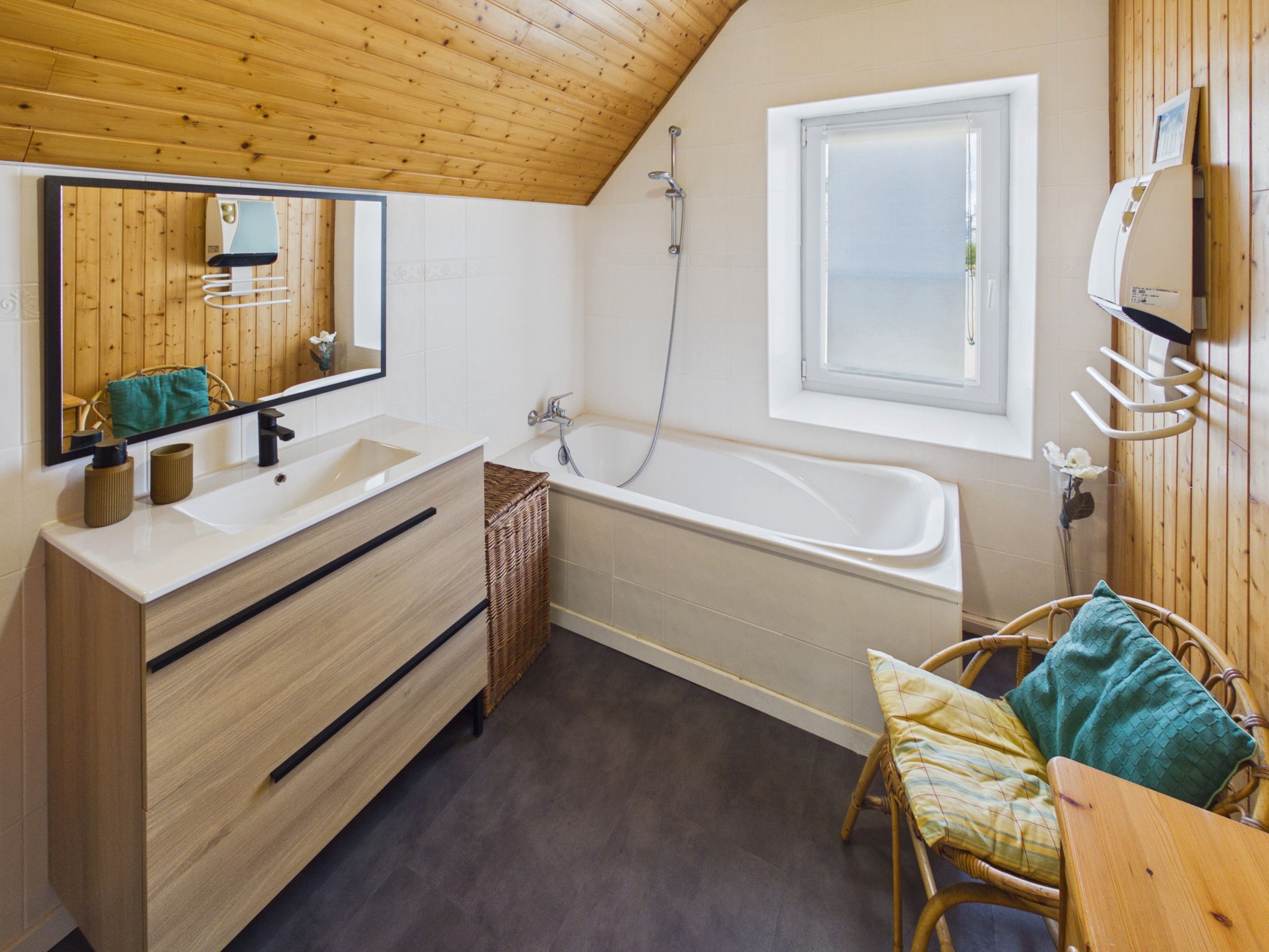 A bathroom with a wooden ceiling, a bathtub, a large mirror, and a wicker chair.