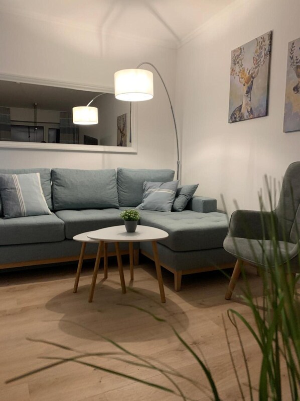 Ein modernes Wohnzimmer mit einem grauen Sofa, einem runden Couchtisch mit einer Pflanze und einer Stehlampe.