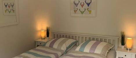 A double bed with striped bedding, two bedside tables with lamps, and wall art above the bed.