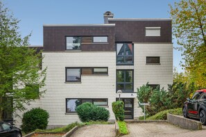Un edificio residencial moderno de varios pisos, con tejado plano, amplias ventanas y una señalización con el número de la dirección visible.