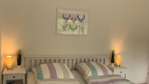 A double bed with striped bedding, two bedside tables with lamps, and a wall-mounted artwork. - Apartment 'Harz 21' with Dreamy Balcony Views (Braunlage)