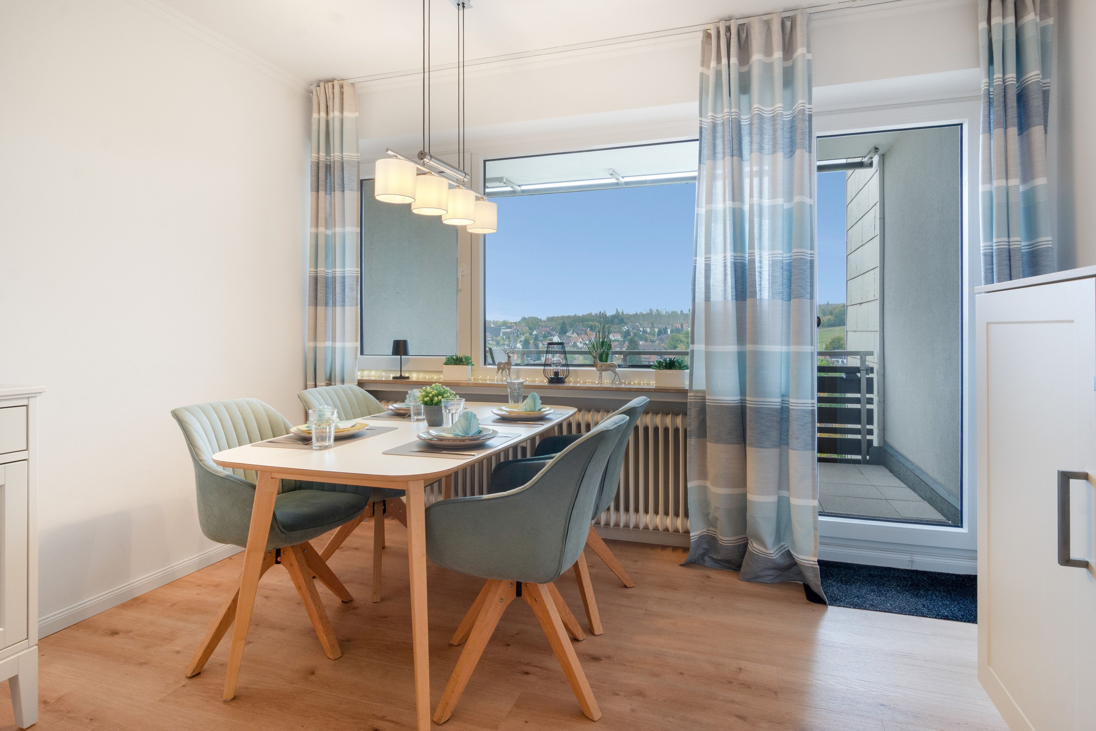 Spiseområde med et bord dækket til fire personer, en radiator og udsigt til et boligområde gennem et vindue.