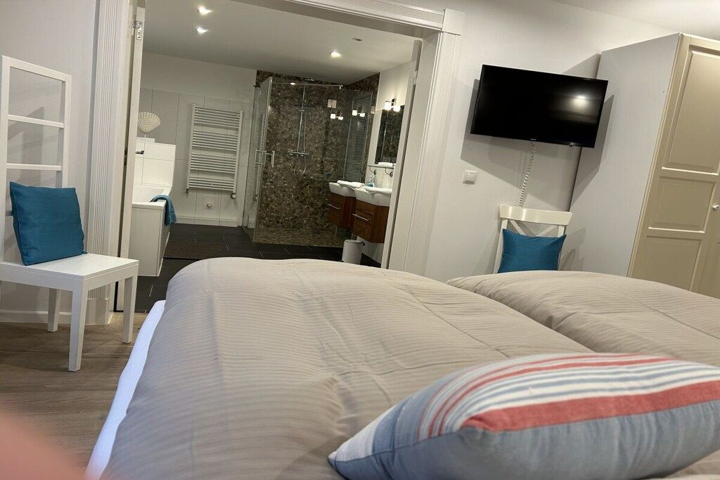 A hotel room with a bed, a TV mounted on the wall, a bathroom with a shower, and a desk with a chair.
