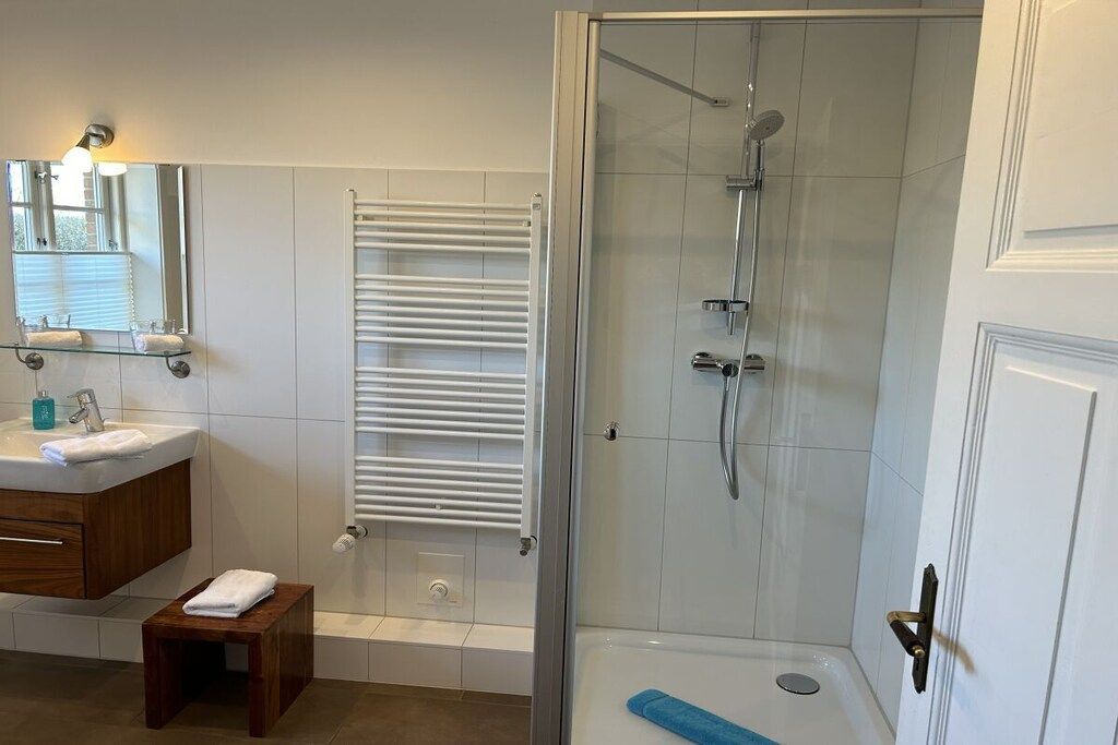 Un baño con cabina de ducha de vidrio, un lavamanos blanco con espejo y un perchero para toallas.