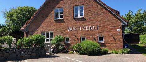 A brick building with the name 'WATTPERLE' on the facade, a stone wall, and a paved driveway.