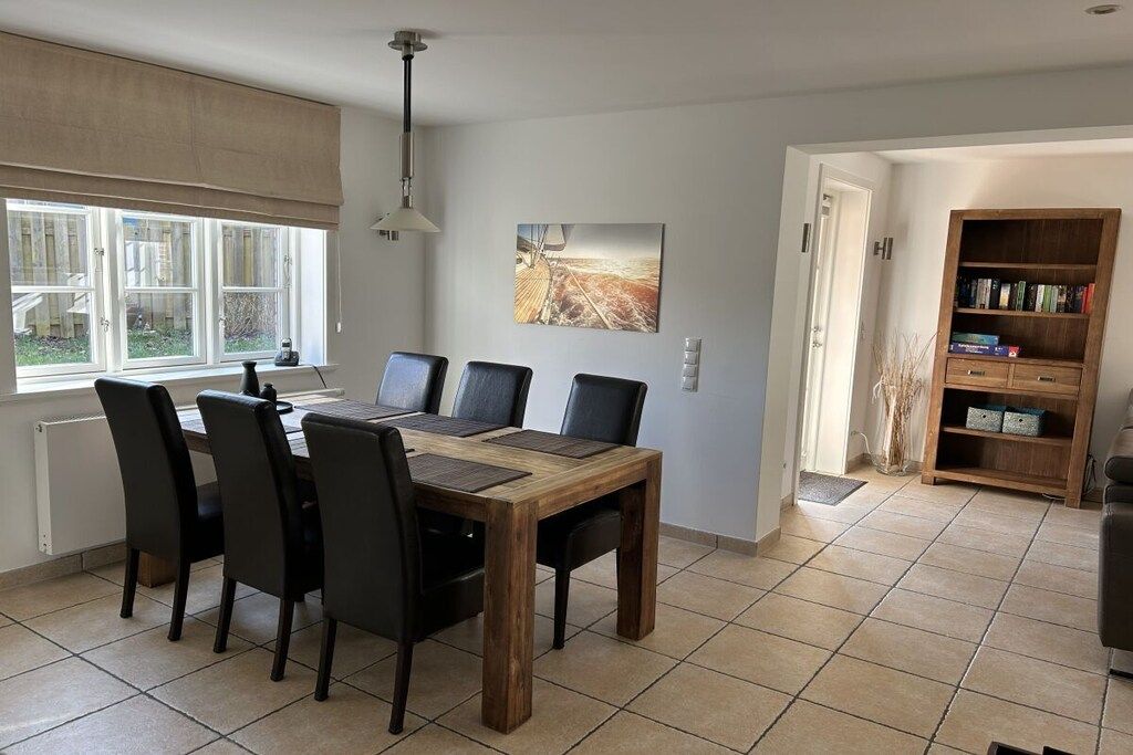 A dining area with a wooden table and chairs, a painting on the wall, and a bookshelf.