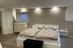 Ein Schlafzimmer mit Bett, Nachttischen, einem Fenster mit Jalousien und einer Tür.