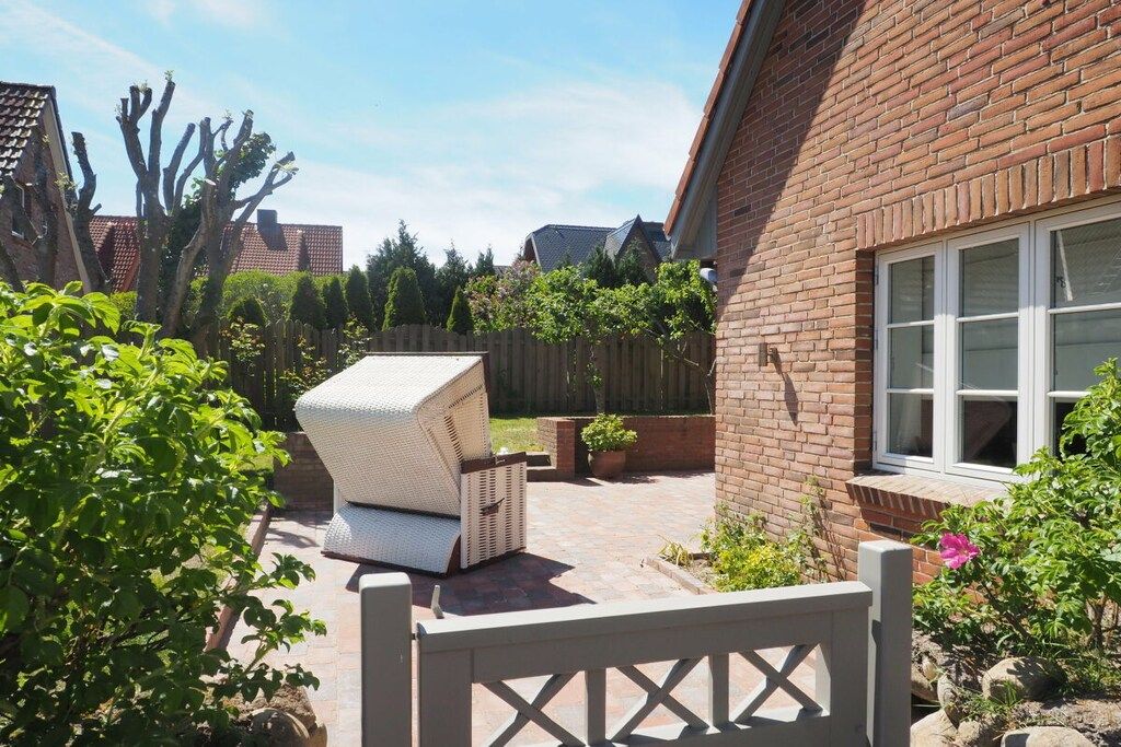 A brick house with a white door, a white chair, and a small garden area with plants and a wooden fence.