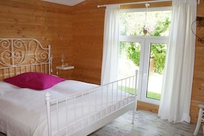 A wooden room with a bed, a window, and a view of greenery outside. - Holiday home Rainbow (Friedrichskoog)