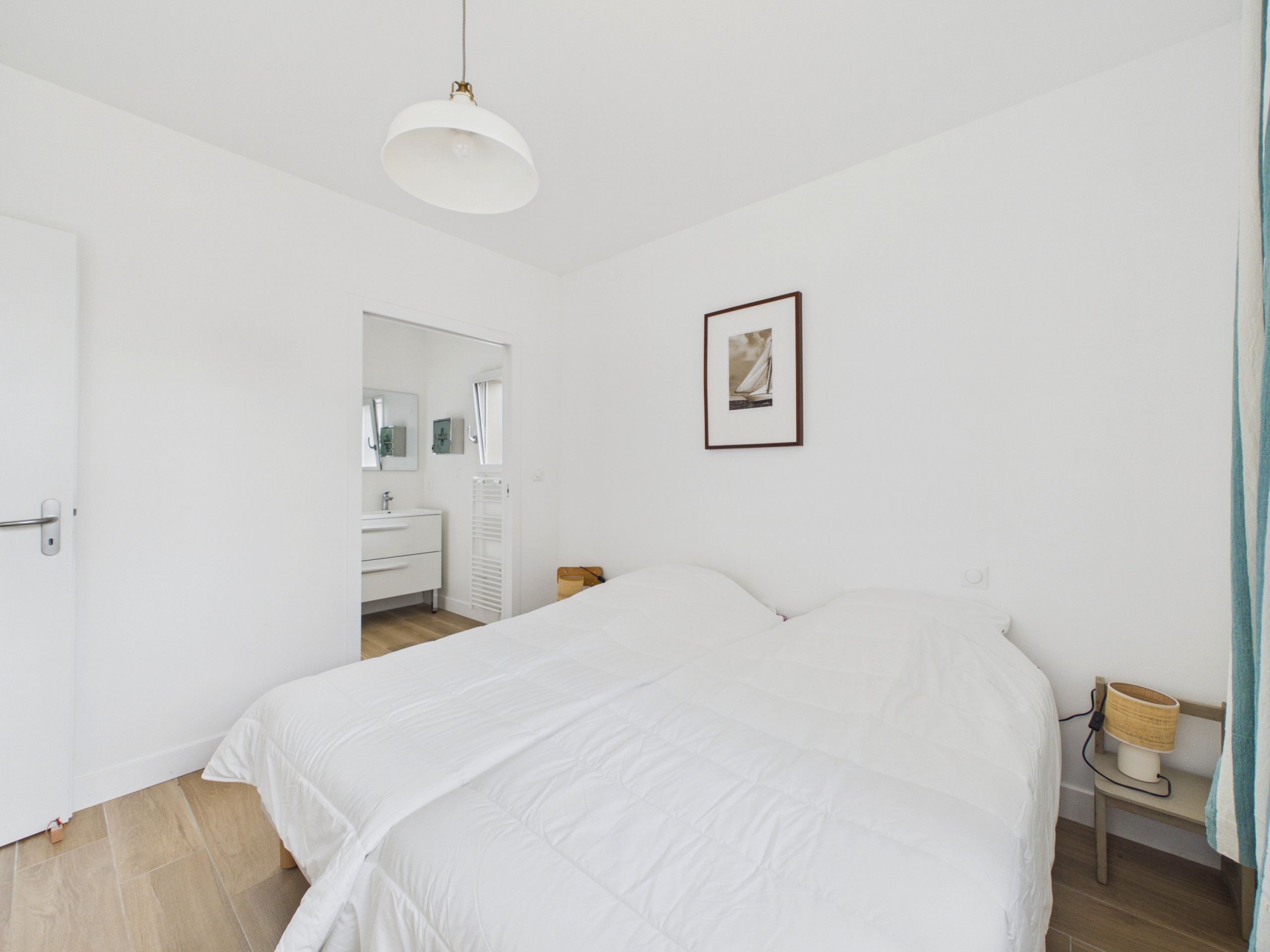 A bedroom with a bed, a bedside table, a lamp, a framed picture on the wall, and a door leading to a bathroom.