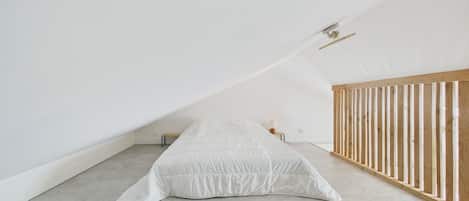 Una habitación minimalista con techo inclinado, una cama individual, una mesita de noche pequeña y una cuna de madera.