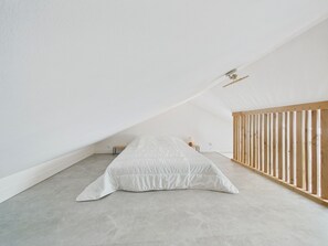 Ein schlichter Raum mit schrägem Dach, einem Einzelbett, einem kleinen Nachttisch und einem hölzernen Wiege.