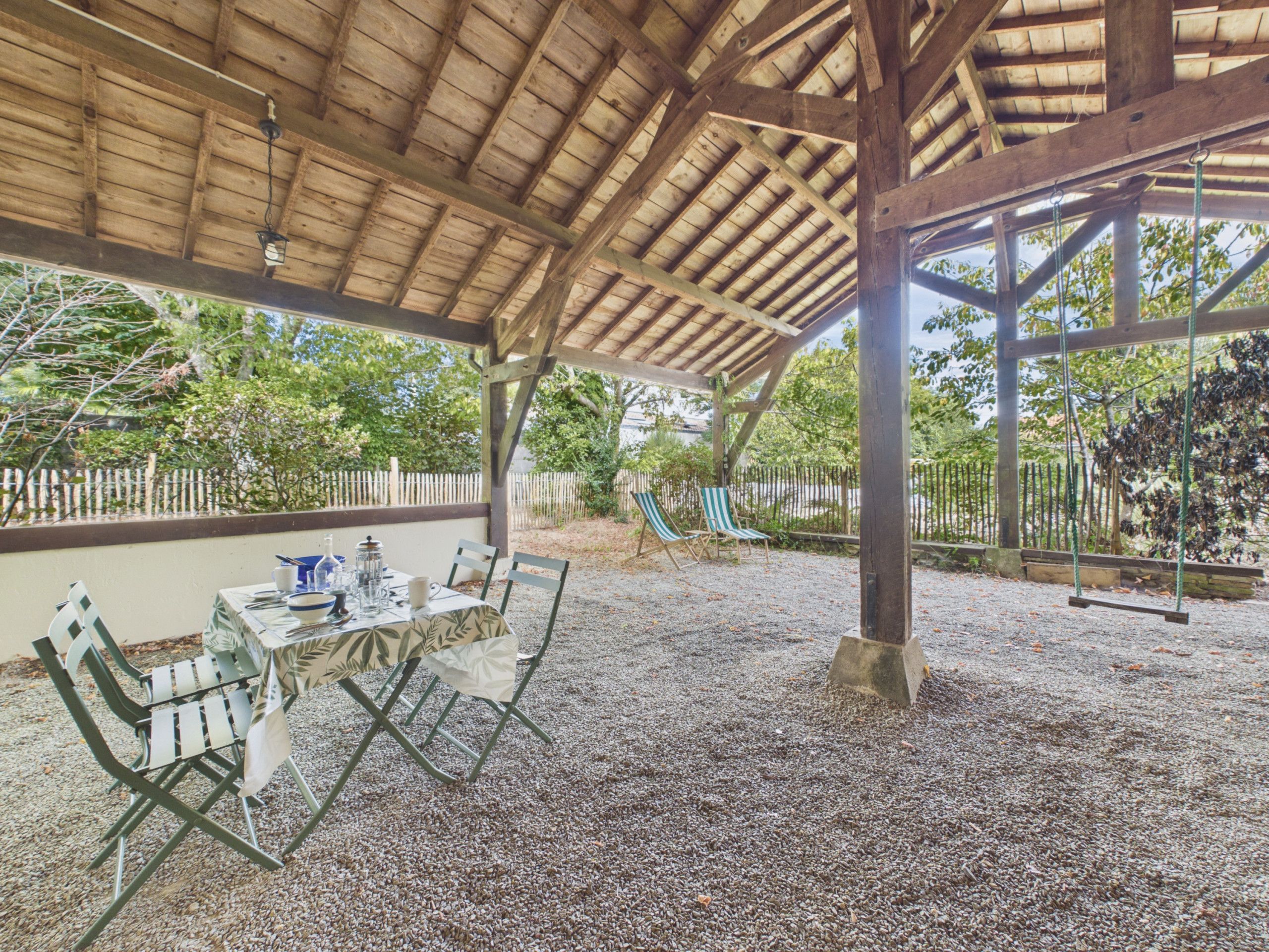 An outdoor covered patio with a table set for dining, surrounded by chairs.